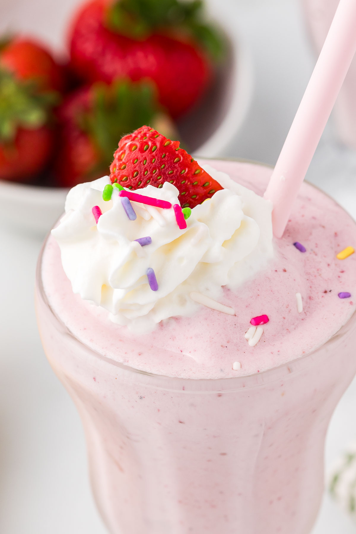 Strawberry banana milkshake with whipped cream a strawberry and some sprinkles.