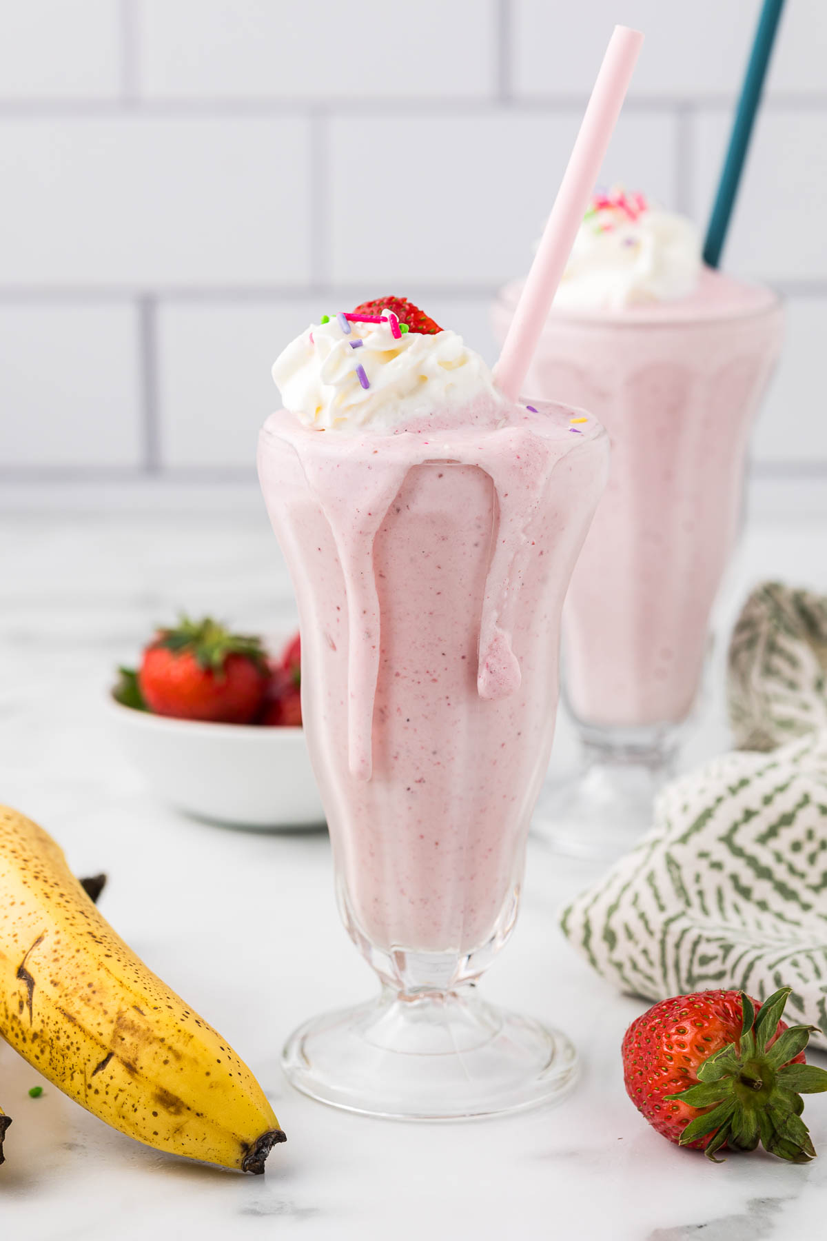 Two Strawberry Banana Milkshakes with whipped topping, sprinkles and a strawberry. 