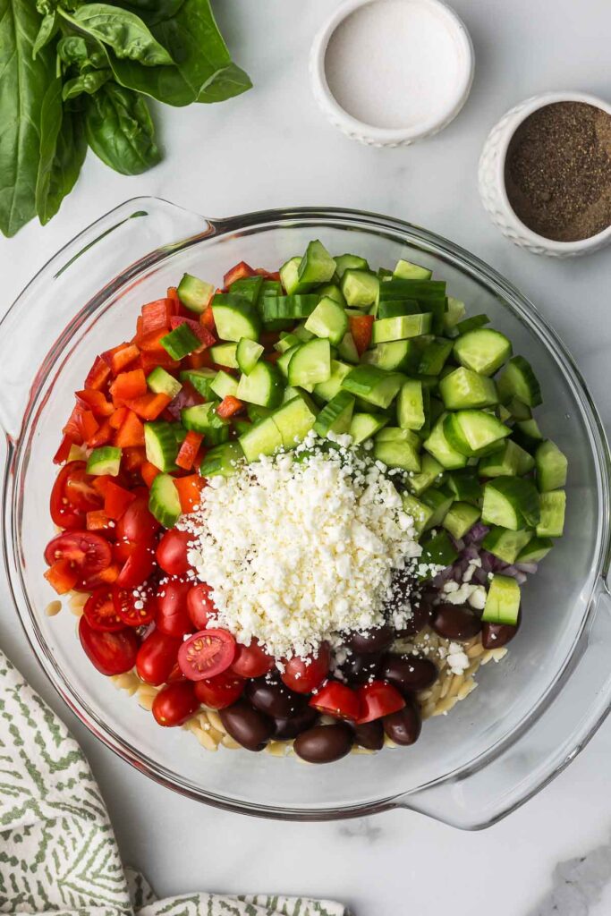 A bowl with orzo, cucumber, red bell pepper, tomatoes, olives and feta cheese.