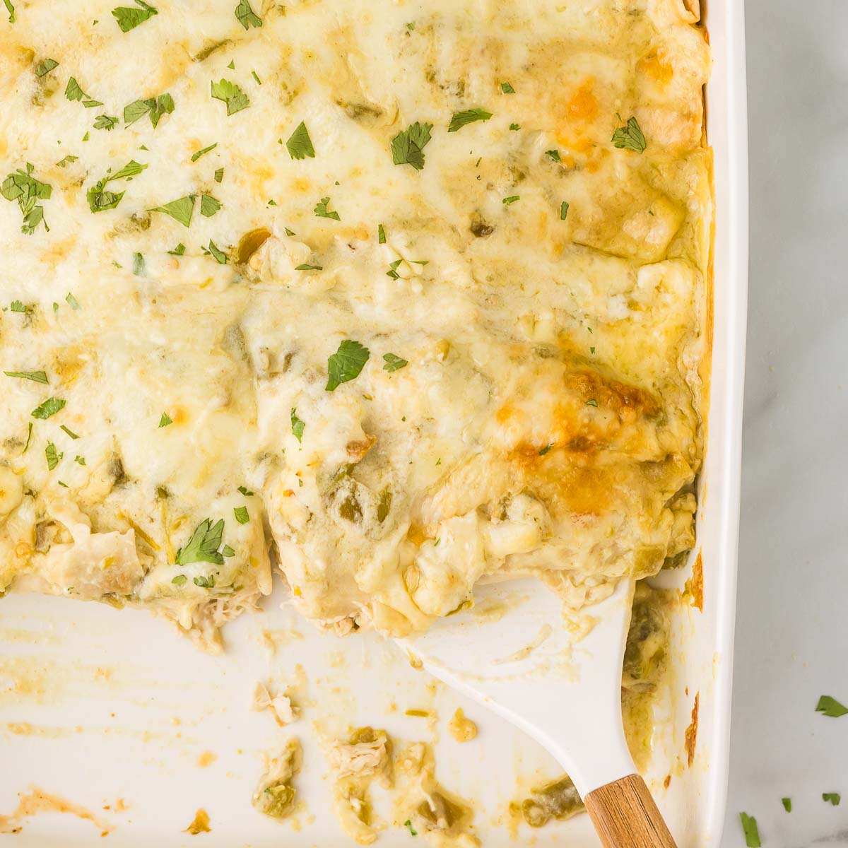 White chicken enchilada recipe in a white casserole dish with a white and wooden spatula.