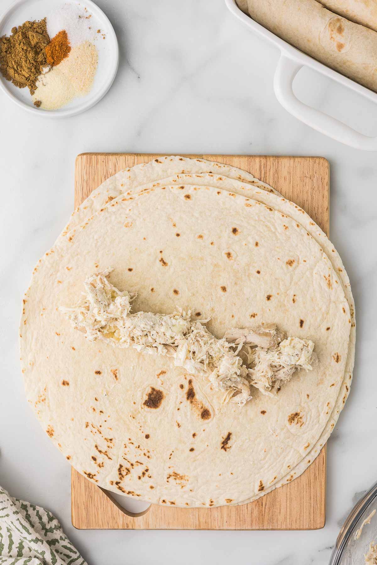 Flour tortilla topped with creamy chicken filling before rolling.