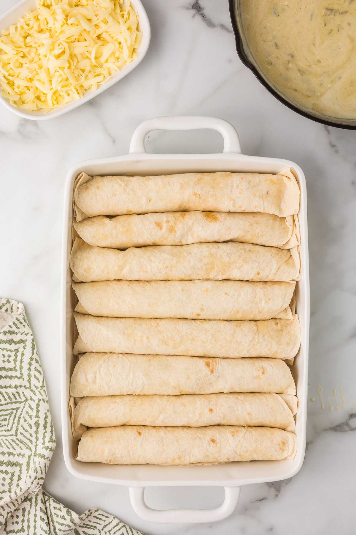 Rolled chicken enchiladas arranged seam-side down in a baking dish.