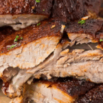 Close-up of tender, juicy slow cooker baby back ribs coated with a brown glaze, garnished with chopped herbs. The text at the top reads "SLOW COOKER BABY BACK RIBS." The bottom shows the website "COOKINGUPMEMORIES.COM.