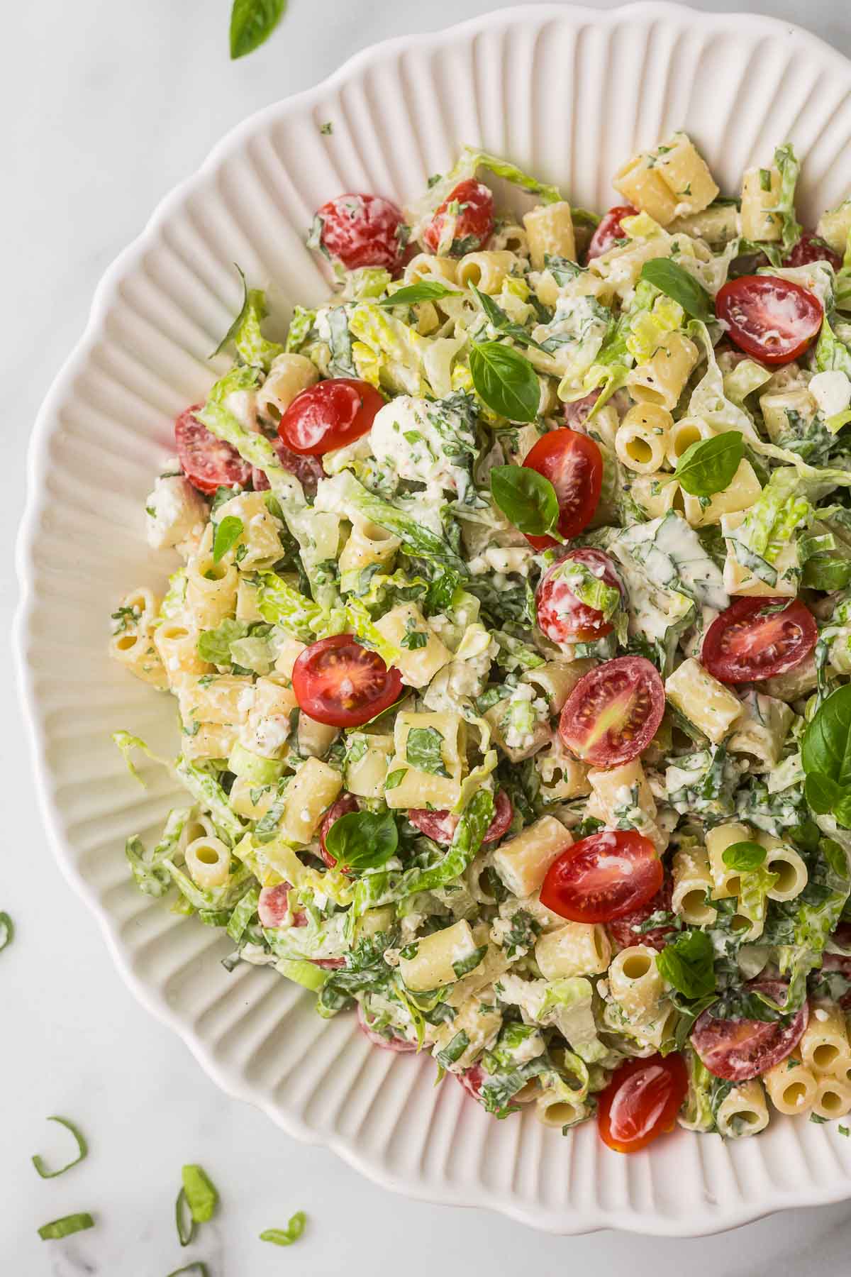 Caesar pasta salad with tomatoes in a white bowl.