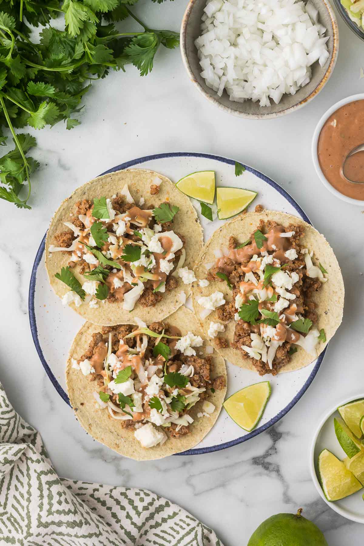 Three pork tacos on a plate with toppings surrounding the plate.