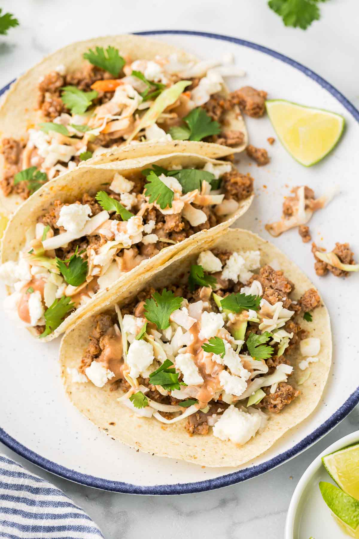 Pork tacos on a plate with toppings including cilantro, cheese and slaw.