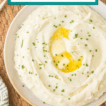 A bowl of creamy Boursin mashed potatoes with a knob of melted butter in the center, garnished with chopped chives. The text reads "Boursin Mashed Potatoes" at the top, and "cookingupmemories.com" at the bottom. The bowl is on a woven mat.