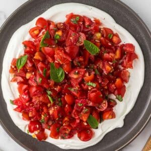 Tomato bruschetta layered over whipped goat cheese with fresh basil leaves.