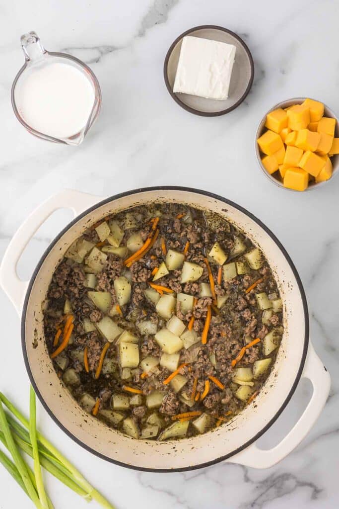 A dutch oven with veggies, broth and potatoes.