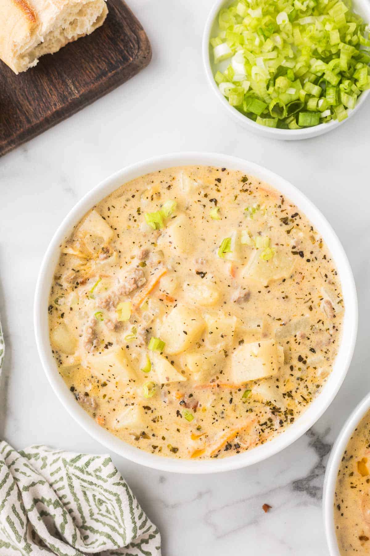 Cheeseburger soup in a white bowl with bread and green onions.