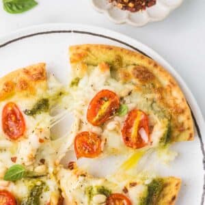 Pesto Chicken Pizza on a plate with red pepper flakes.