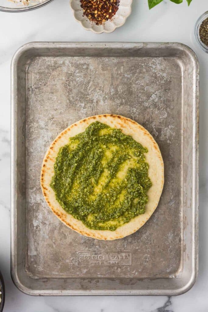 A top down view of a flatbread with pesto spread over the top.