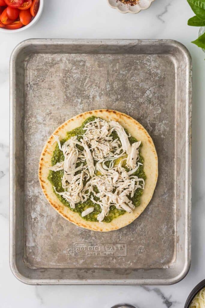 A top down view of a flatbread with pesto and mozzarella cheese over the top before baking.