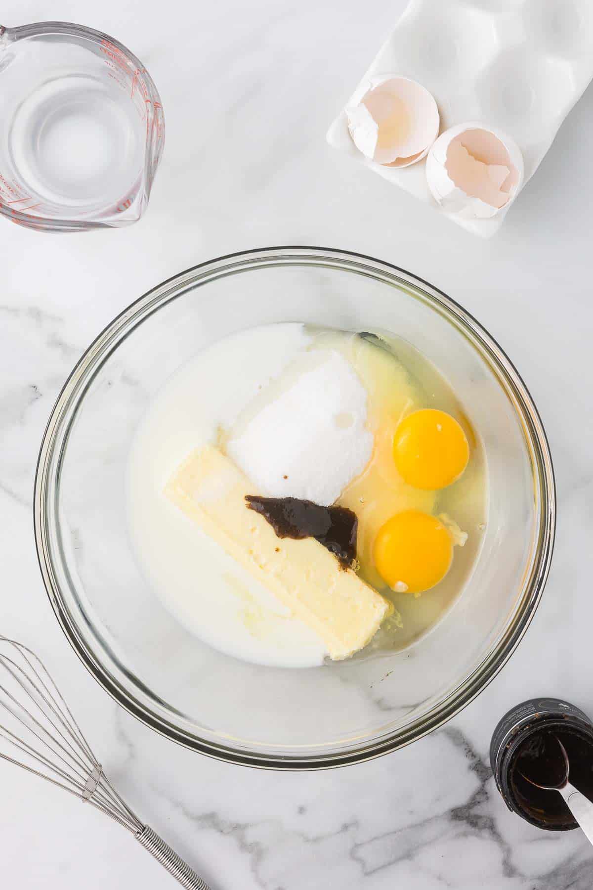 Eggs, sugar, butter, vanilla bean paste in a clear bowl.