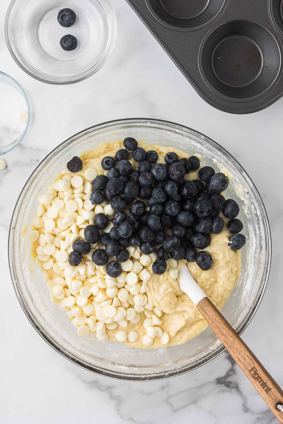 Blueberries and white chocolate chips being added to muffin batter.