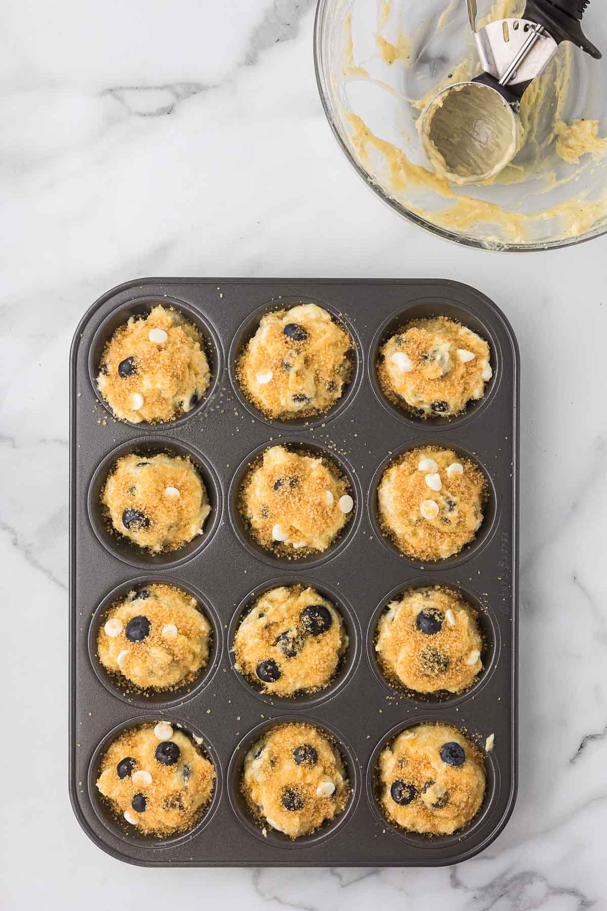 Muffin batter in a muffin pan with cane sugar sprinkled over the top before baking.