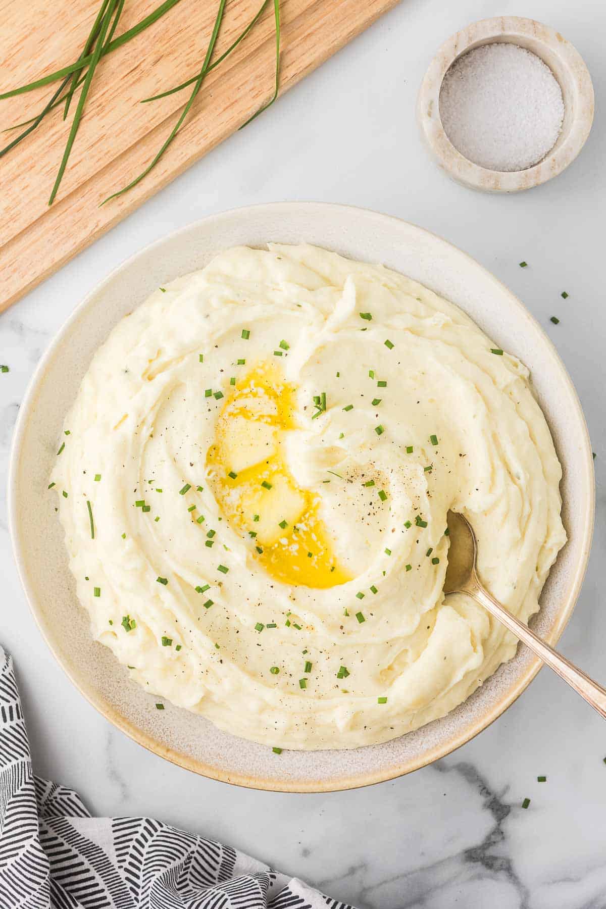 Mashed potatoes with boursin cheese ready to serve with chopped chives and butter in a serving bowl.