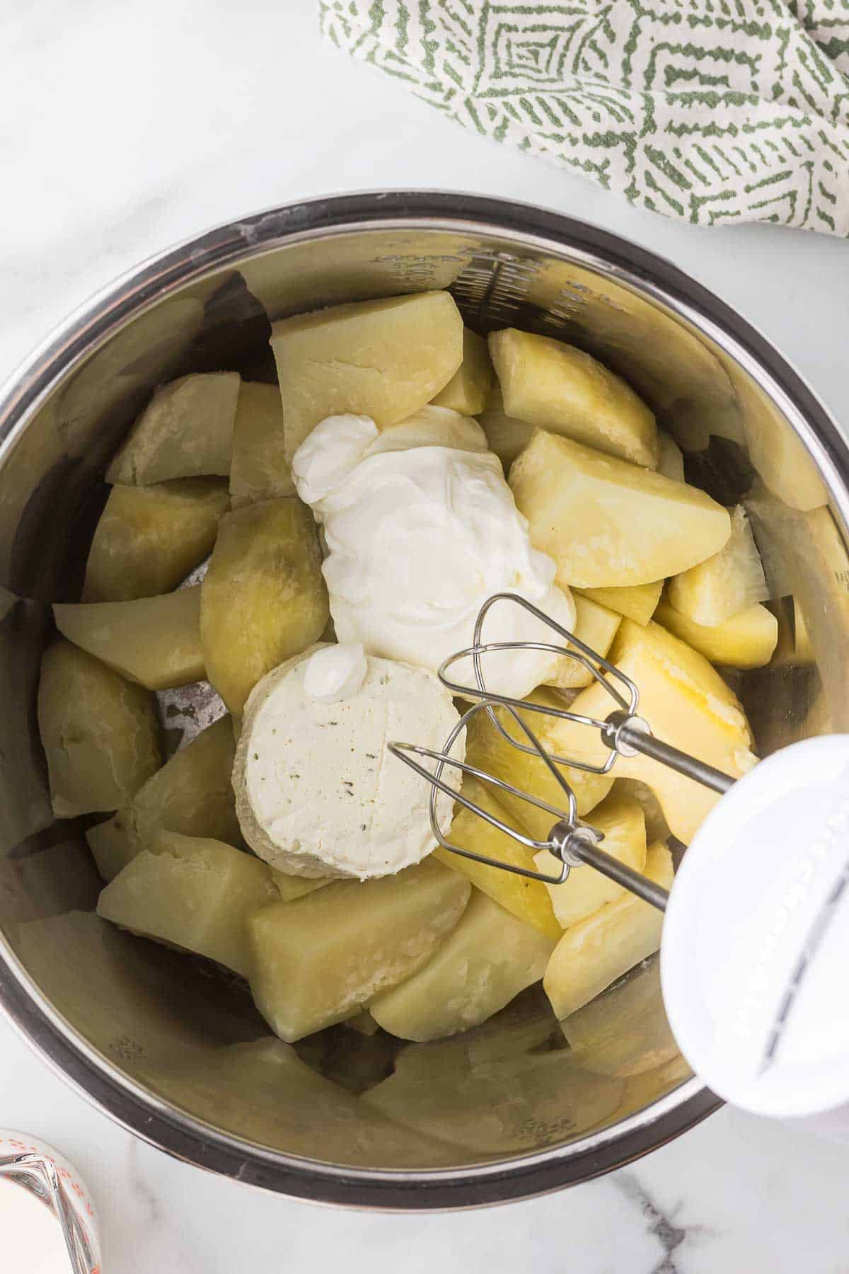 Quartered potatoes after they have been cooked in the instant pot with butter, Boursin cheese and sour cream and a hand mixer getting ready to mix everything.