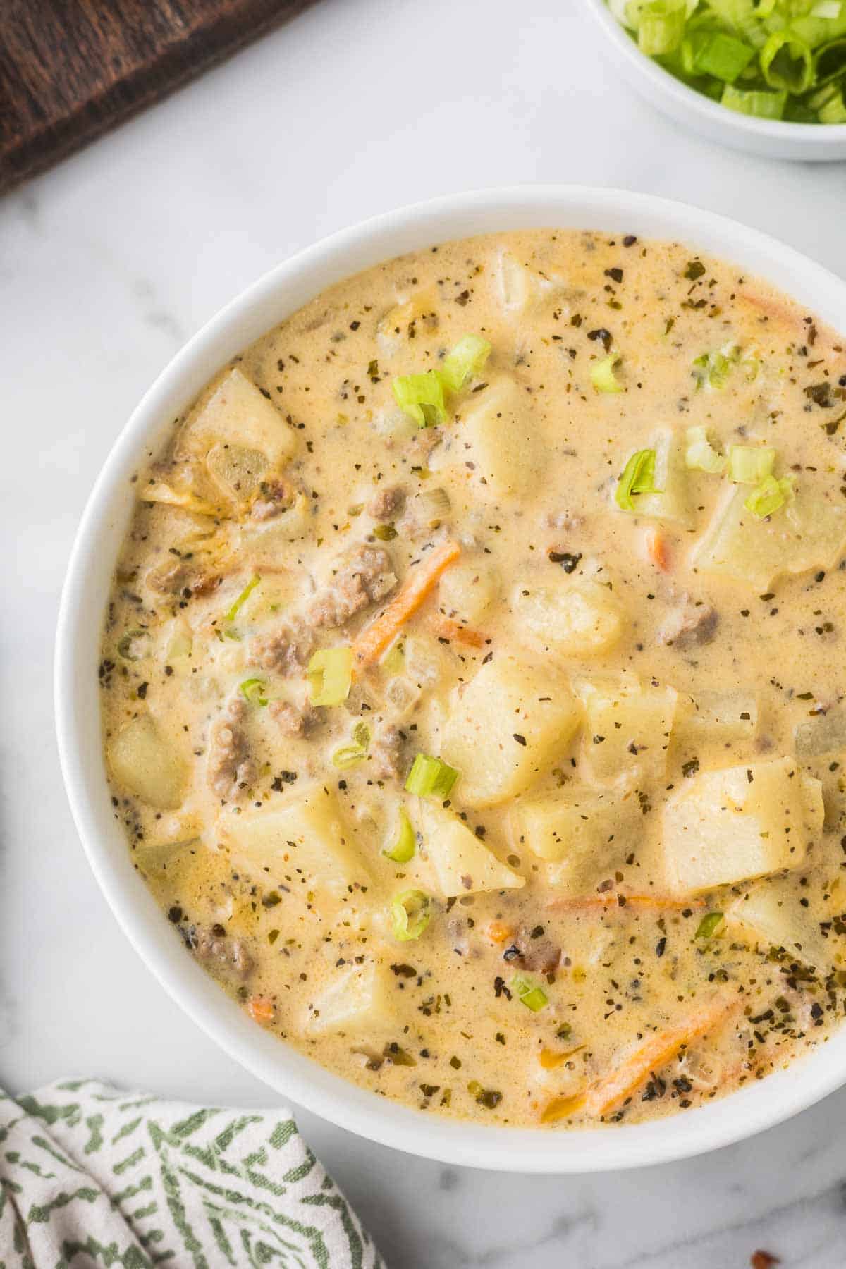 Cheeseburger soup in a white bowl with a green and white linen.