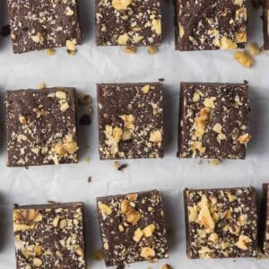 Overhead view of multiple squares of chocolate walnut fudge topped with chopped nuts, arranged neatly on parchment paper.