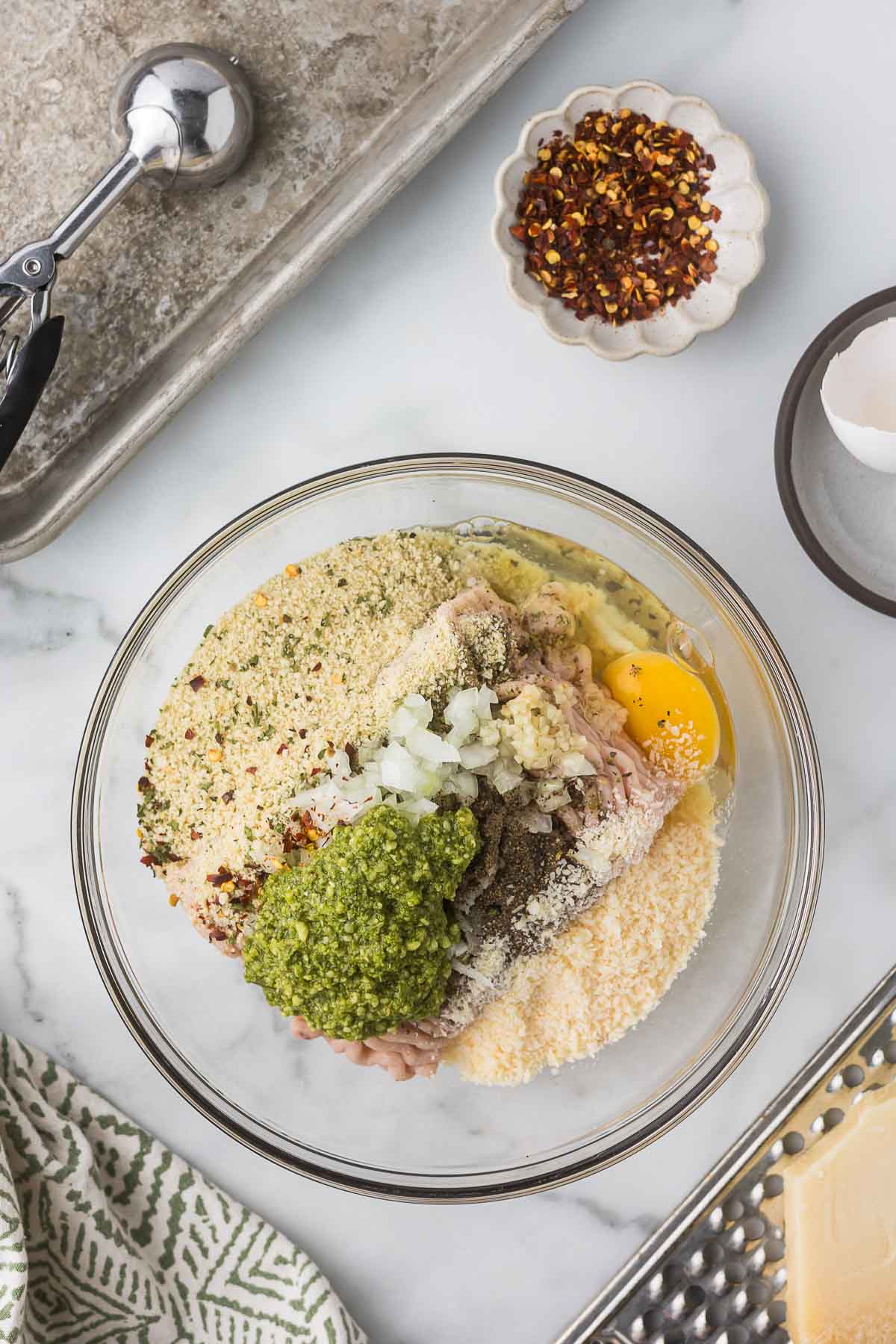 All the ingredients for chicken meatballs with pesto in a glass bowl before mixing.