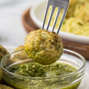 Pesto Chicken Meatball being dipped into a small bowl of pesto.