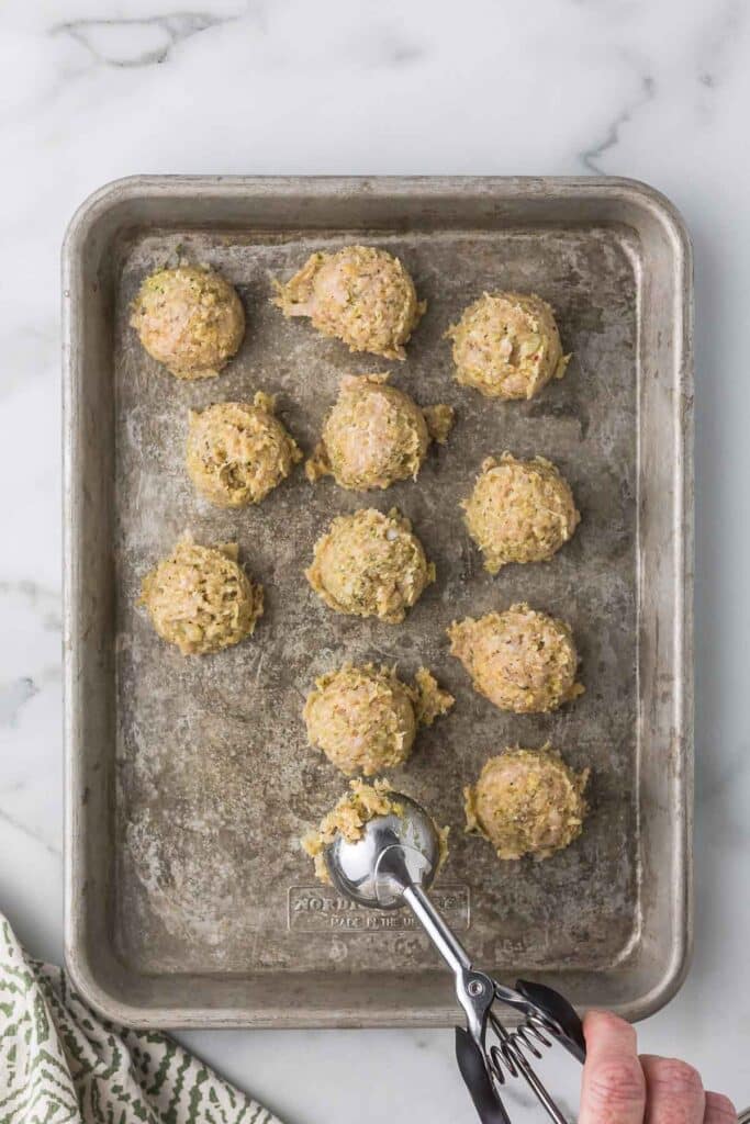 Pesto chicken meatballs being placed on a baking sheet using a cookie scoop.