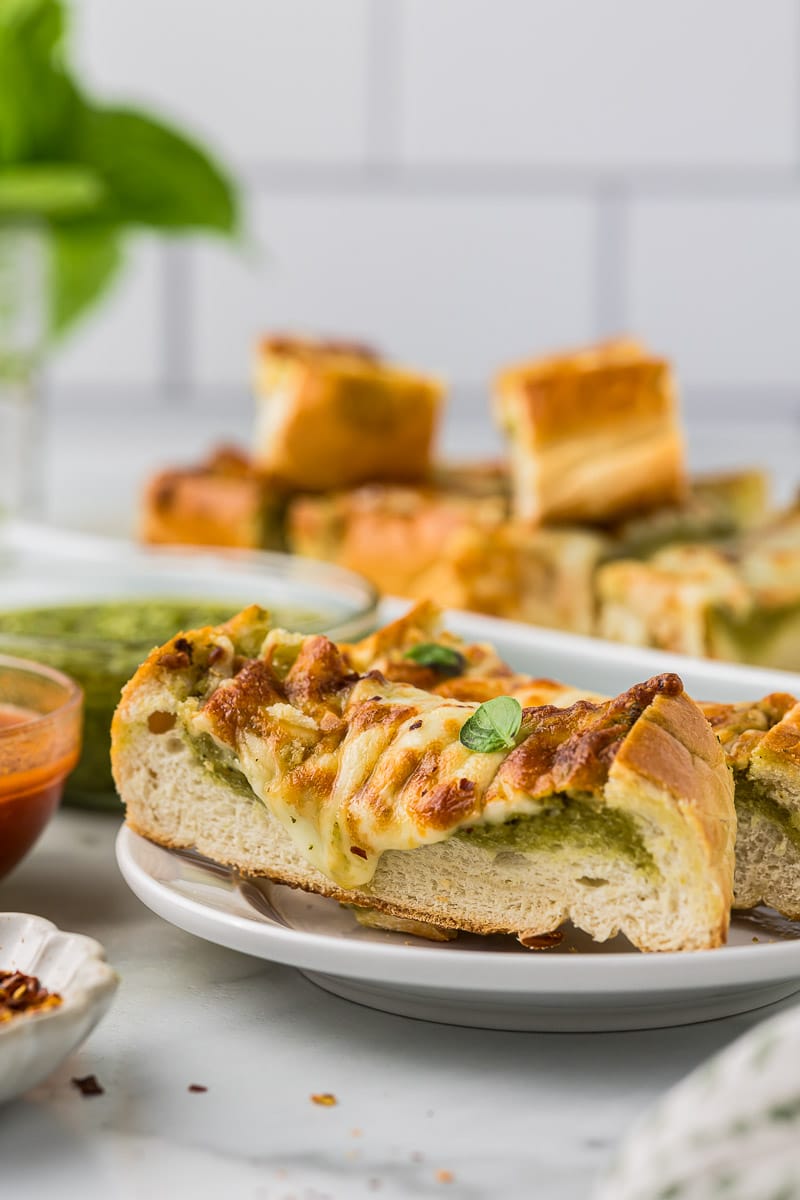 Pesto garlic bread cut into pieces on a white plate.