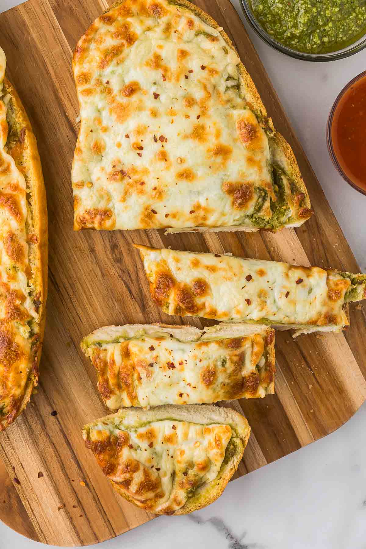 Garlic Bread with pesto and cheese sliced on a cutting board.