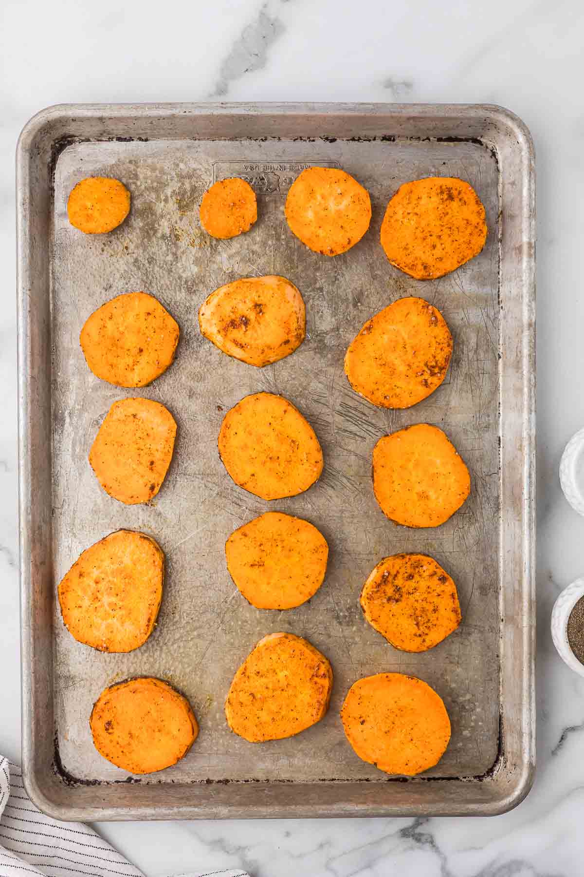 Seasoned sweet potatoes on a sheet pan before baking.