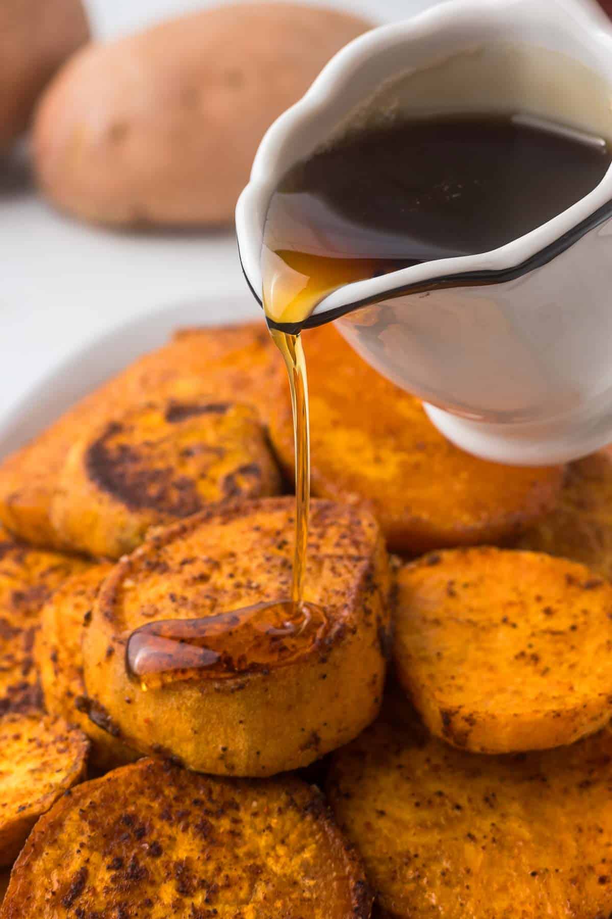 Roasted sweet potatoes with maple syrup being poured over the top.