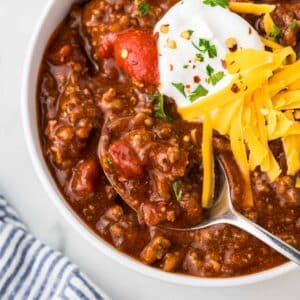 Slow cooker no bean chili in a bowl with a spoon and sour cream and cheddar cheese as garnish.