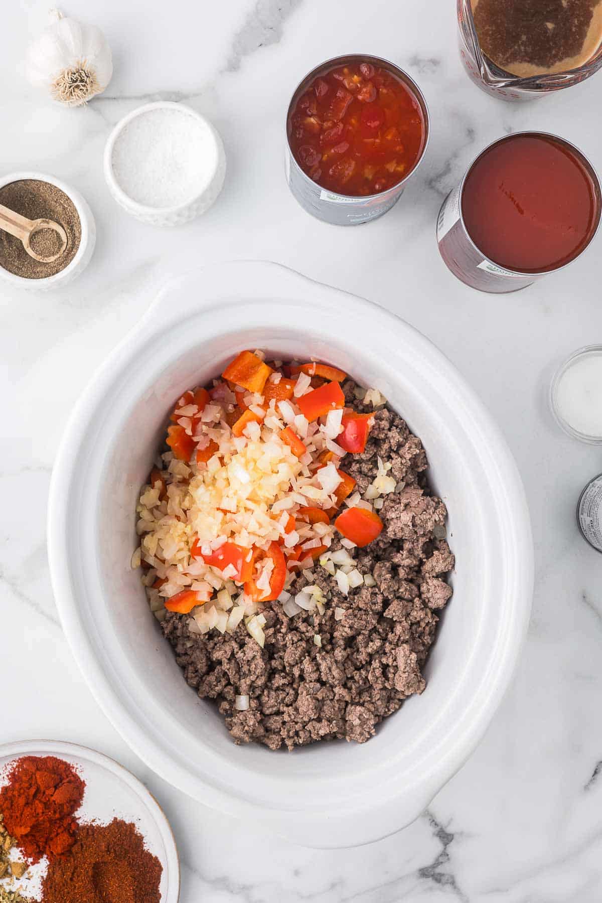 Ground beef, onions, red bell peppers, and garlic in a crock pot to make chili.