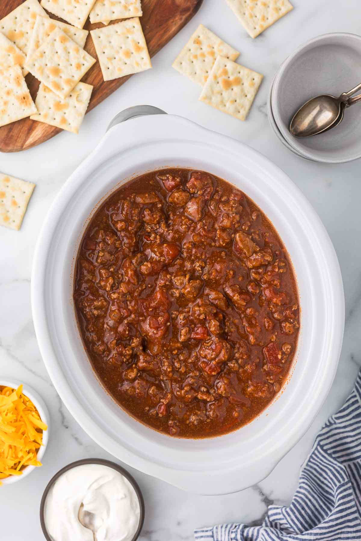 Slow cooker chili without beans with crackers, cheddar cheese and sour cream for serving.