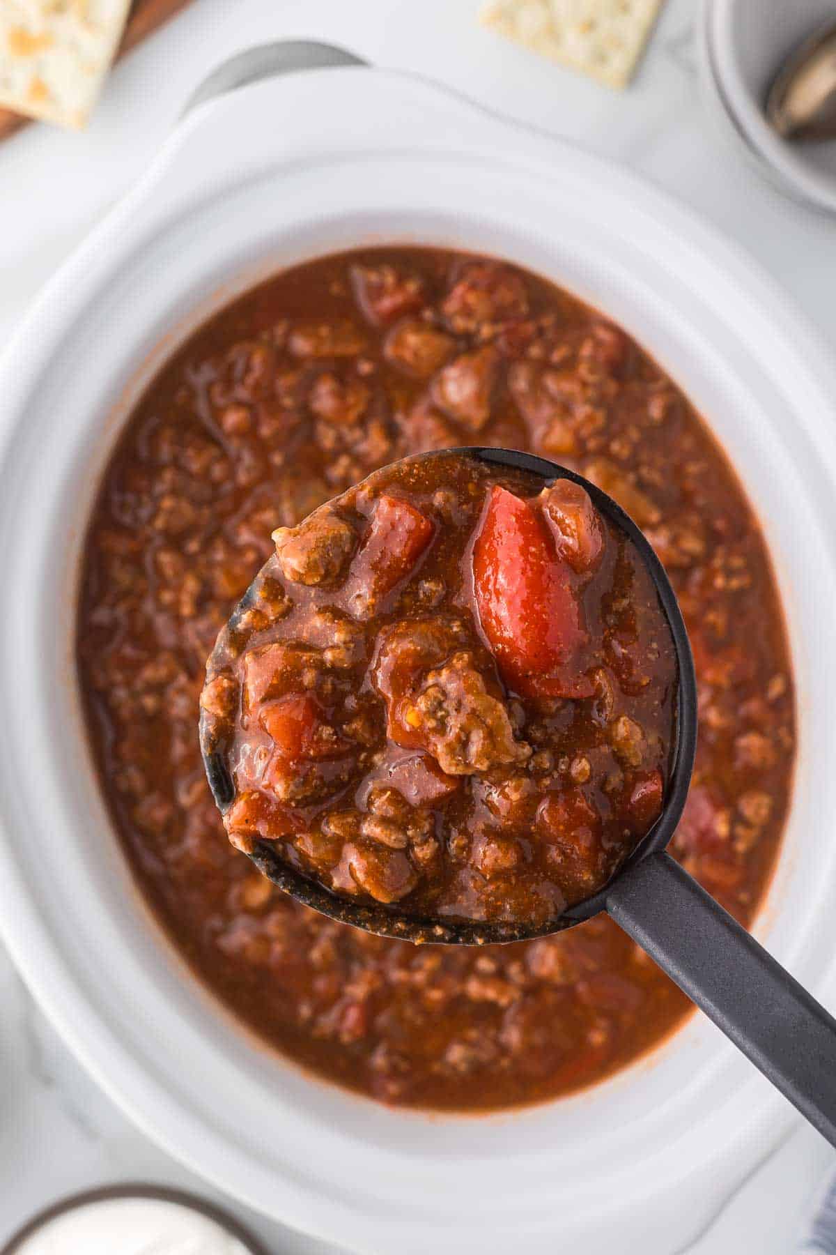 A ladle of chili above a white crock pot.