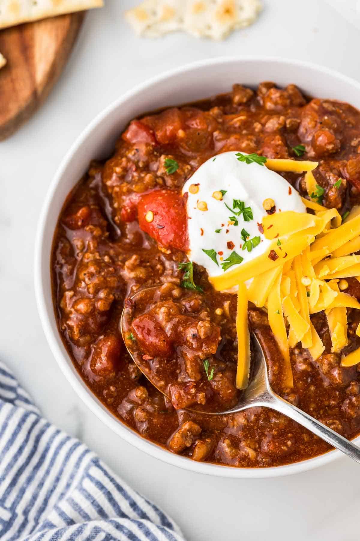 A bowl of no bean chili that was made in the slow cooker with a spoon, sour cream and cheddar cheese.