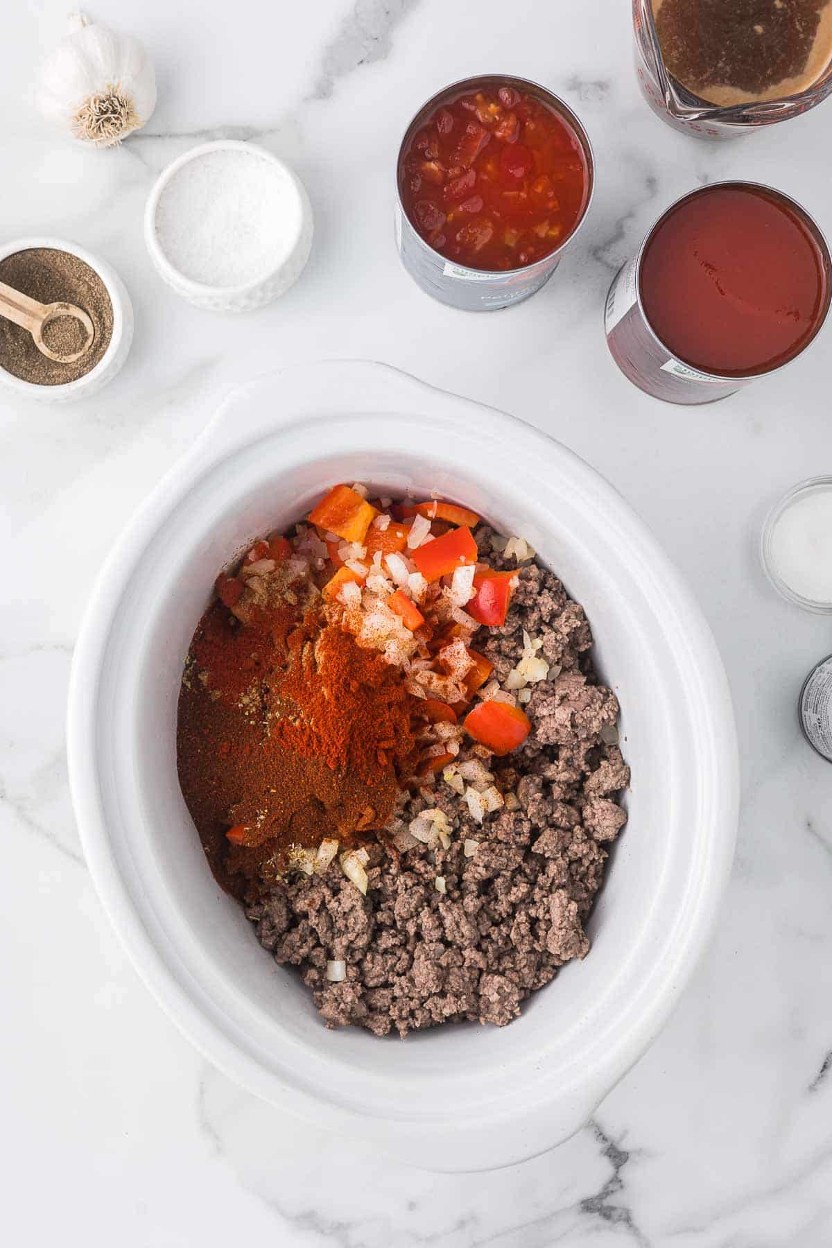 Ground beef, onions, red bell peppers, garlic and spices in a crock pot to make chili.