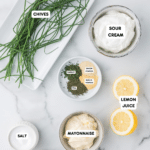 Image of ranch dressing ingredients artfully arranged on a marble surface, featuring chives, sour cream, lemon juice, and other essentials like parsley and dill. Each ingredient is labeled with the same care as a chocolate chip butterscotch cookie recipe.