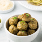 A bowl of chicken pesto meatballs garnished with basil leaves sits enticingly next to plates of pasta and grated cheese. It's a feast for easy meals, almost as irresistible as a tempting slice of chocolate walnut fudge.