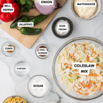 Top-down view of coleslaw ingredients on a marble surface, with labeled items like coleslaw mix, mayonnaise, sour cream, sugar, vinegar, cumin, and more. While chocolate chip butterscotch cookies are absent here, the vibrant spread includes corn, cilantro, bell pepper, jalapeno, and onion.