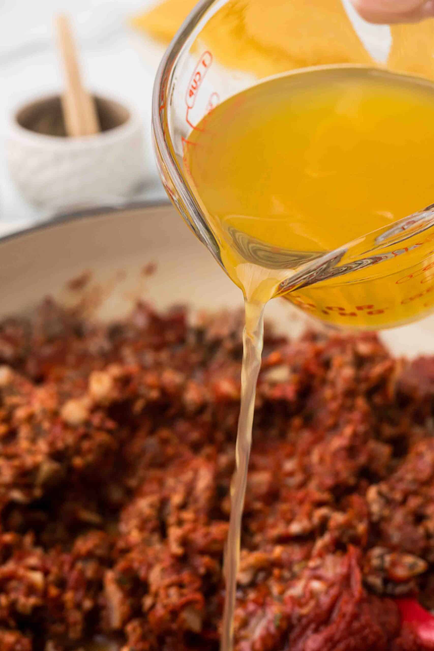 Broth being poured into the skillet of meat. 