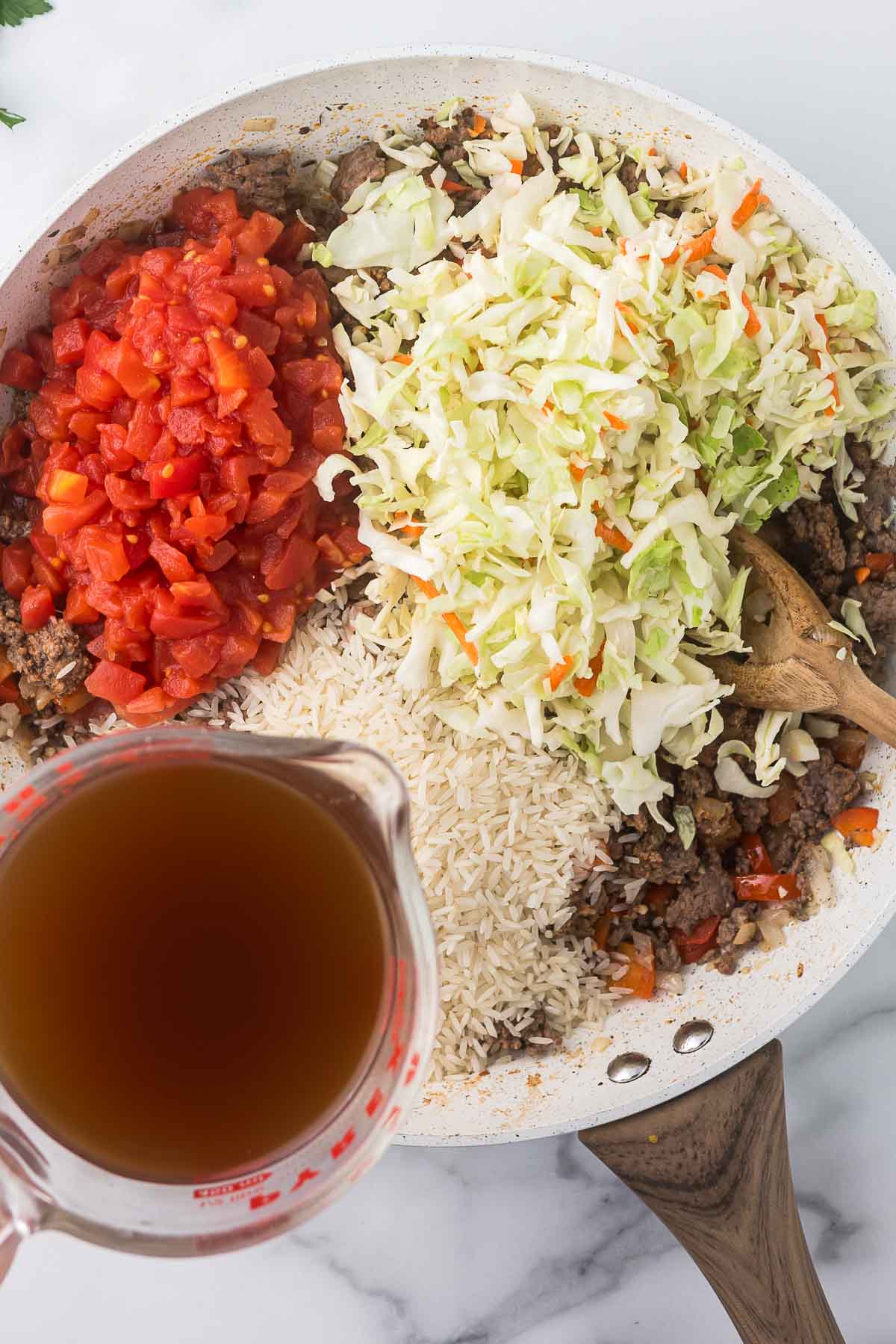 A pan filled with ground meat, diced tomatoes, raw rice, and shredded cabbage. 