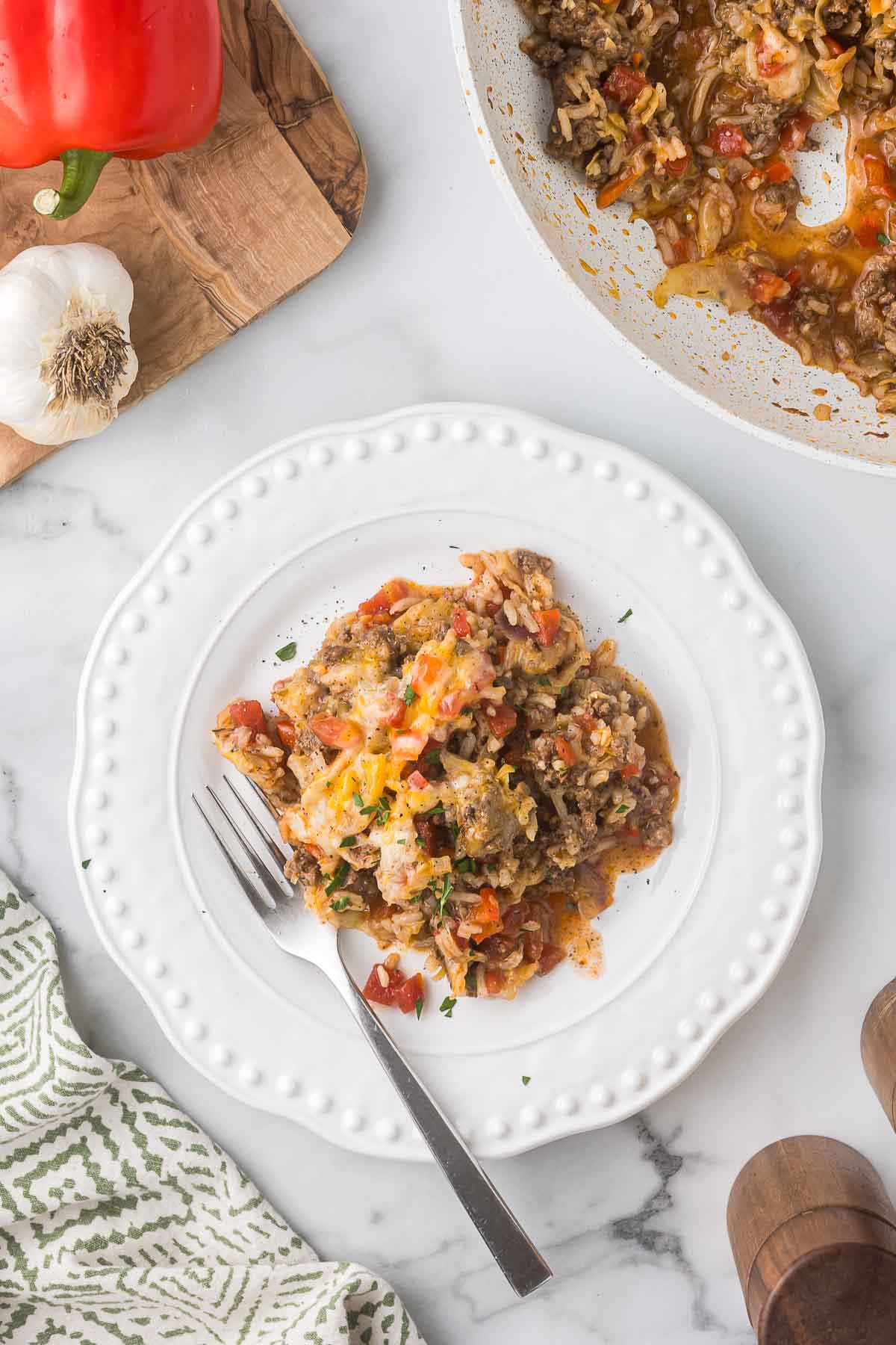 A white plate with a serving of stuffed pepper casserole, featuring ground beef, rice, tomatoes, and melted cheese. 