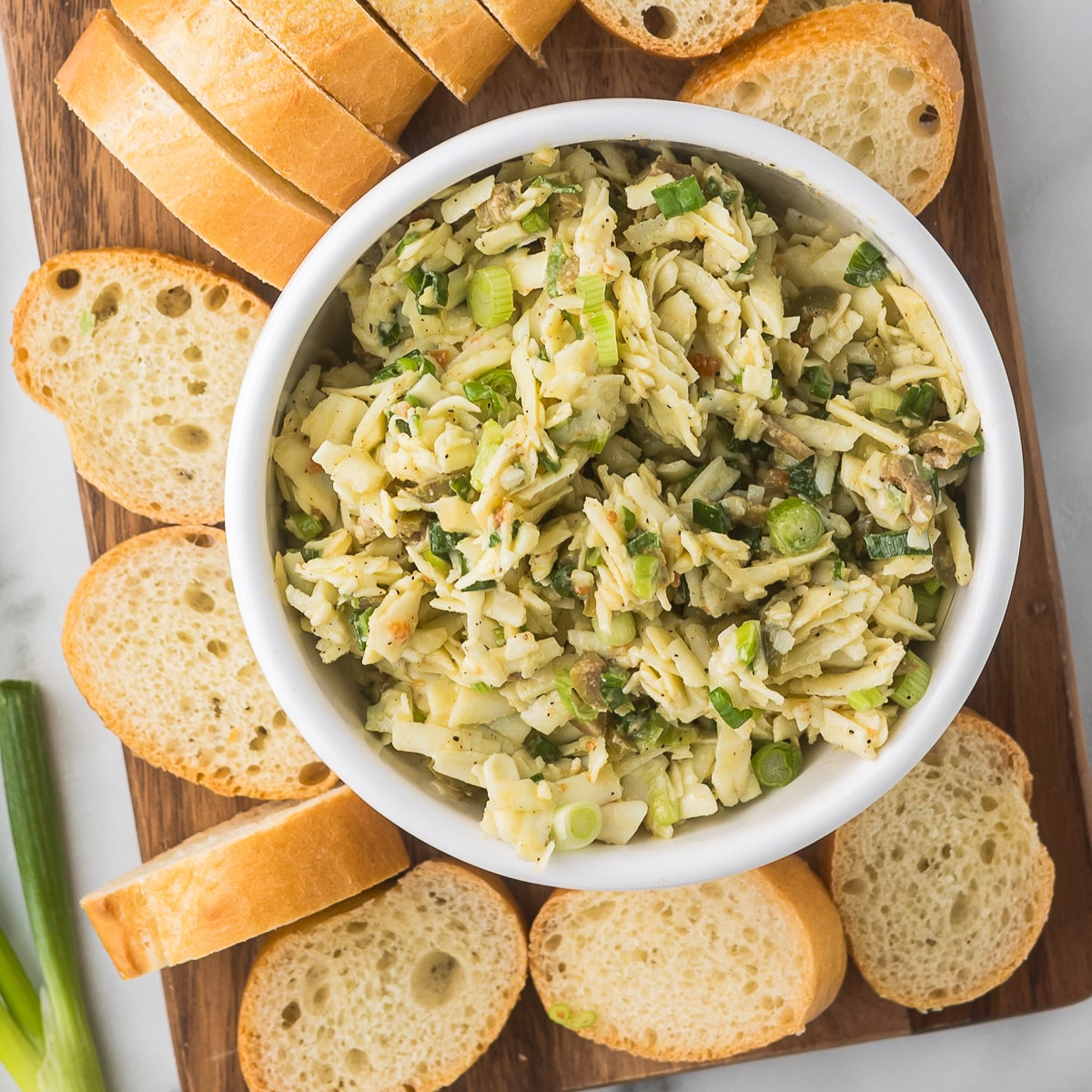 Zesty Gruyere Dip in a white bowl with bread on a cutting board.