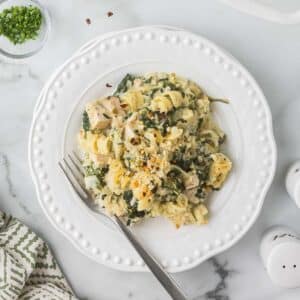 Spinach artichoke chicken pasta o a white plate with a fork.