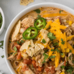 A bowl of cream cheese chicken chili topped with shredded cheese, sliced jalapeños, tortilla strips, and cilantro. The dish includes chicken, corn, and tomato in a creamy sauce. Text on the image promotes a stove-top recipe available at a website.