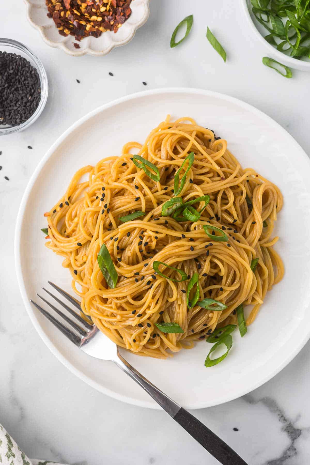 Asian noodles garnished with black sesame seeds and green onions.