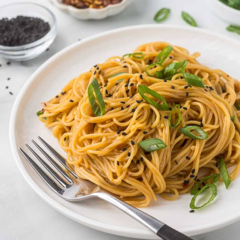 Asian noodles on a white plate with a fork and green onions as garnish.