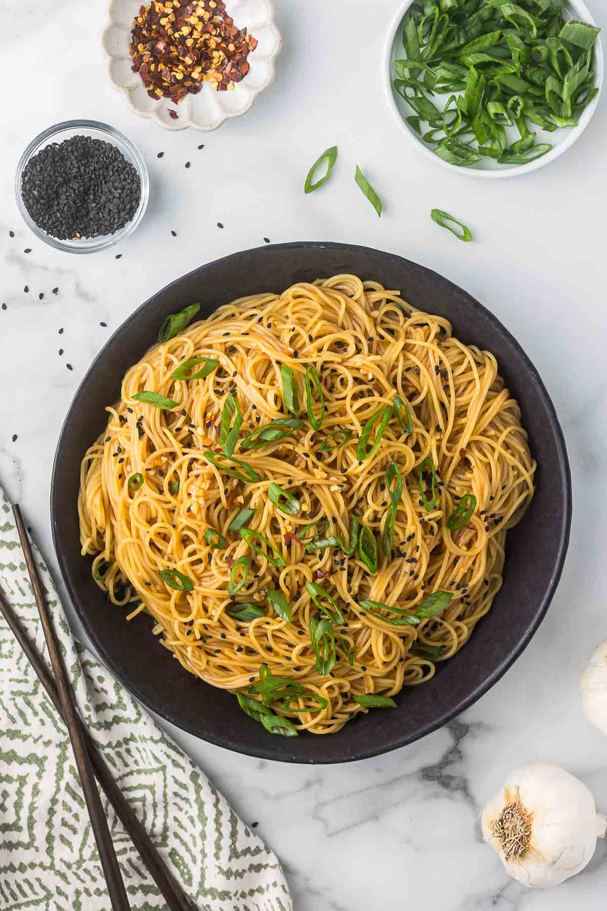 Garlic Asian Noodles in a black bowl with scallions, black sesame seeds and red pepper flakes.