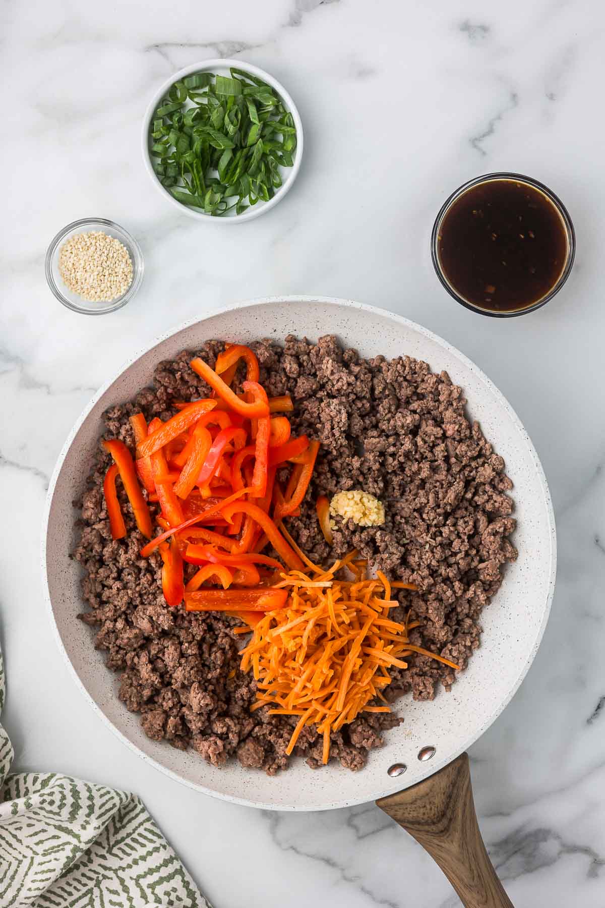 Ground beef with carrots, red bell pepper and garlic being mixed in a skillet.